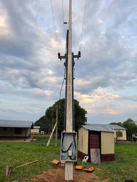 Poste de concreto com caixas e componentes elétricos em área gramada