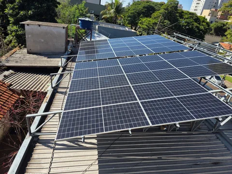 Vista superior de módulos solares com árvores e prédios ao fundo